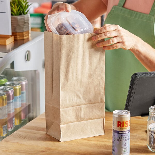 A woman putting food in a Choice natural kraft paper bag on a counter.