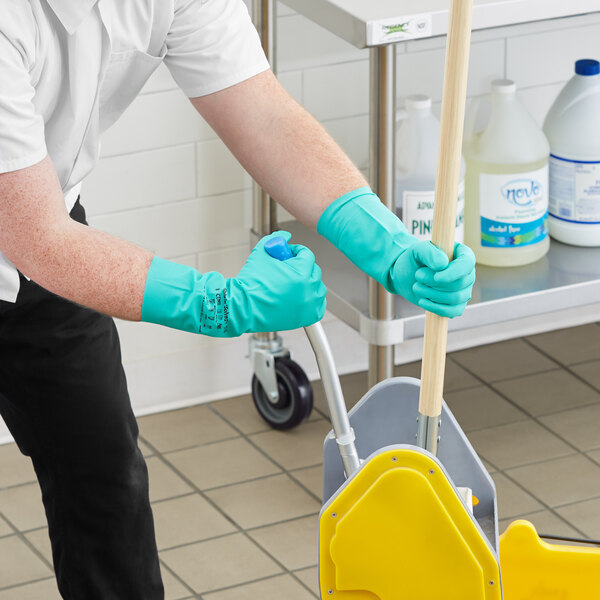 A man wearing green Ansell AlphaTec Solvex gloves is cleaning the floor with a mop.