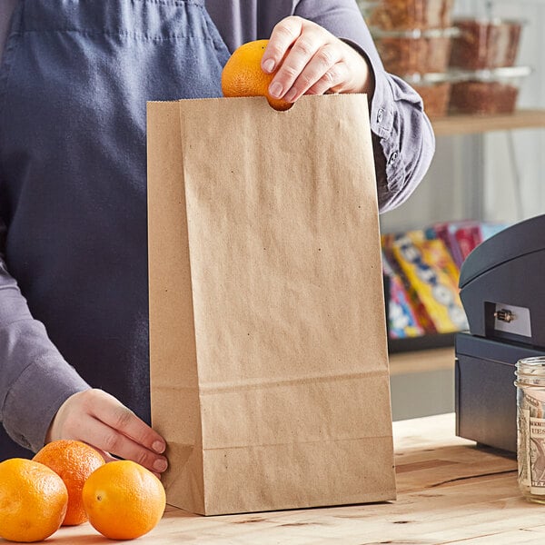 A person holding a Choice natural kraft paper bag with oranges.