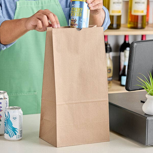 A person putting a white and blue can into a ChoiceHD shorty natural kraft paper bag.