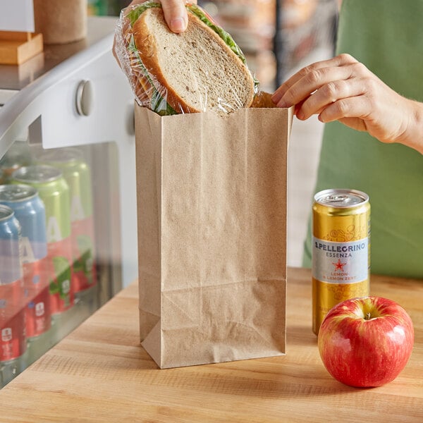 A hand putting a sandwich in a Choice brown paper bag.