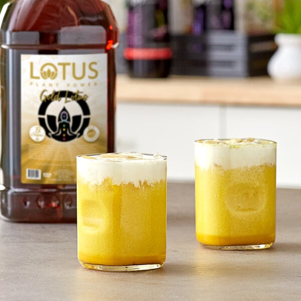 A bottle of Lotus Plant Power Skinny Sugar-Free Gold Lotus Energy Concentrate with two glasses of yellow liquid.