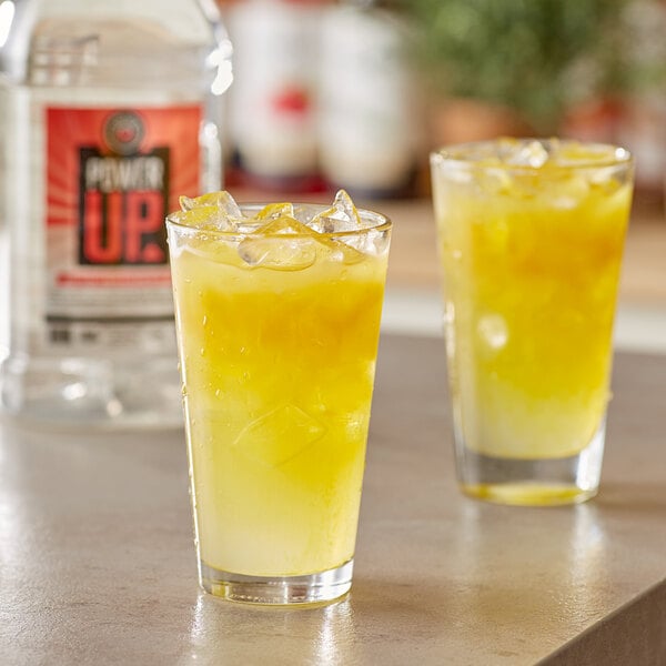 Two glasses of yellow Lotus Plant Energy with ice on a counter.