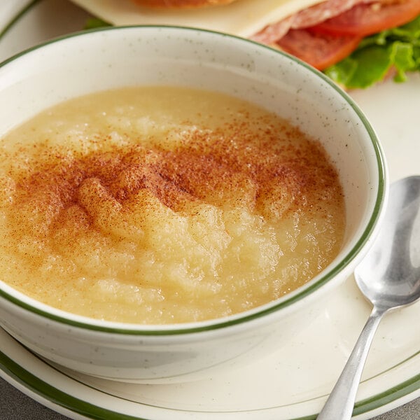 A bowl of Mott's applesauce with a spoon and sandwich on a plate.