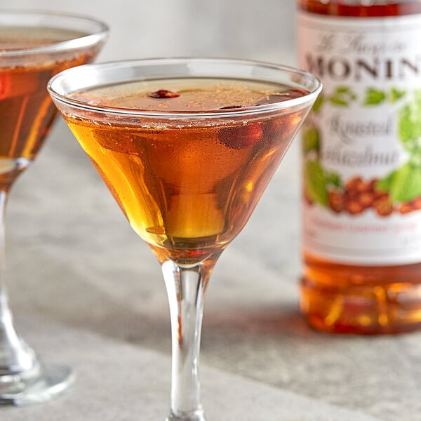 A glass of Monin hazelnut flavored liquid next to a bottle.