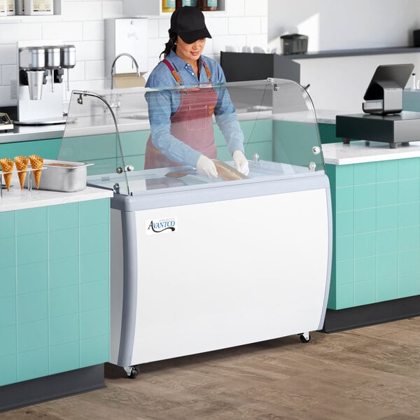 A woman in a blue apron working at an Avantco gelato dipping cabinet.