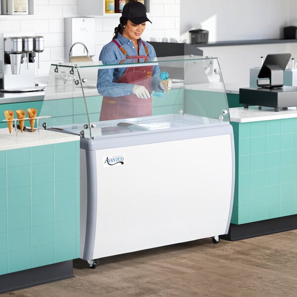 An aproned woman standing behind a white Avantco gelato dipping cabinet.