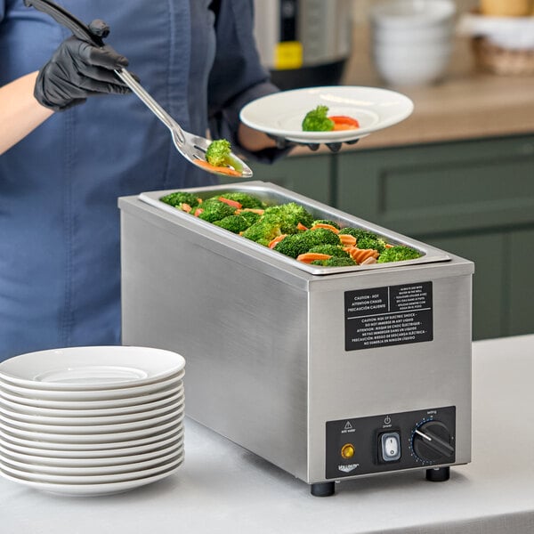 A stainless steel half size countertop food warmer filled with vegetables, used for serving hot food.