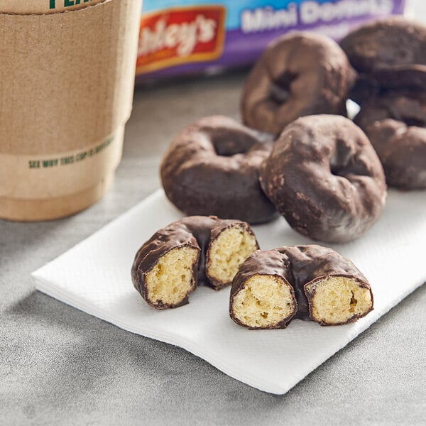 A group of Mrs. Freshley's chocolate frosted mini donuts on a napkin next to a cup of coffee.