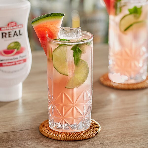 A glass of watermelon and lime juice with a bottle of Real Watermelon Puree Infused Syrup on a table.