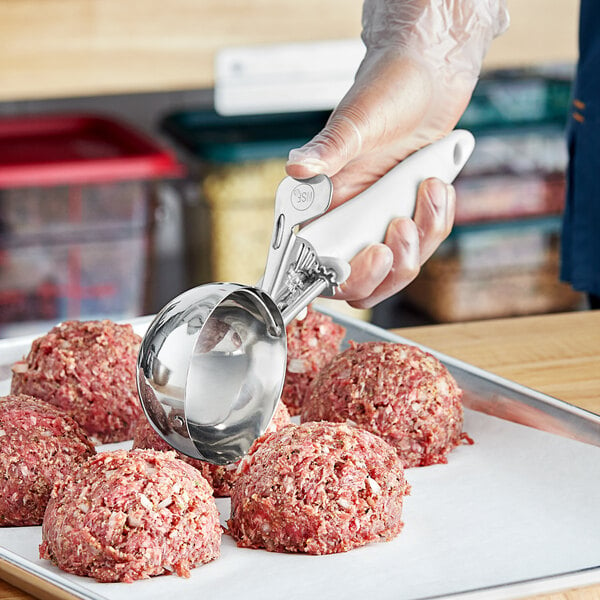 A person using a white Choice thumb press scoop to make meatballs.