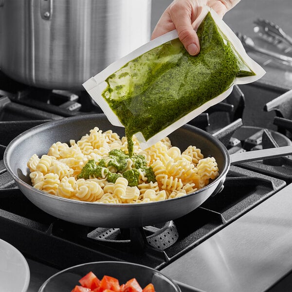 A person pouring Armanino basil pesto into a bowl of pasta.