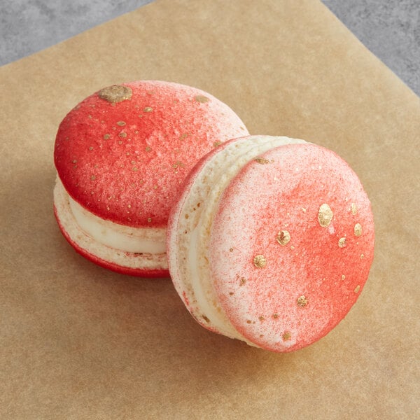 Two Macaron Centrale macarons on a brown surface with gold sprinkles.