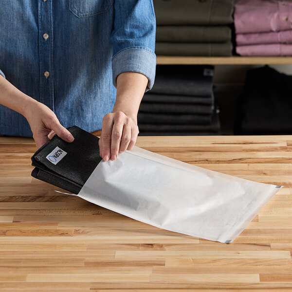 A person putting a white Vela layflat shipping bag into a box.