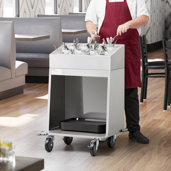 A man in a red apron standing next to a ServIt cart with white containers of utensils.