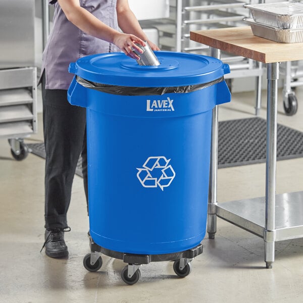 A woman in a blue uniform standing next to a blue Lavex recycling can with a bottle lid.