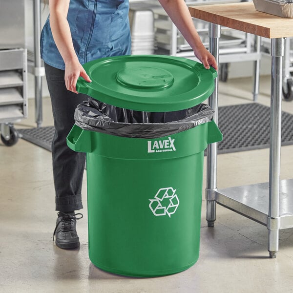 A woman putting a green trash bag into a Lavex green recycling can.