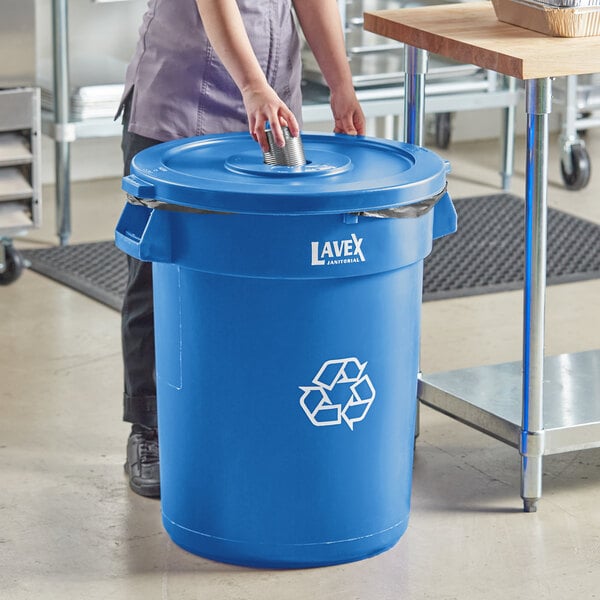 A woman putting a bottle lid on a blue Lavex recycling can.