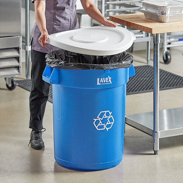 A woman putting a white lid on a Lavex blue recycling can.