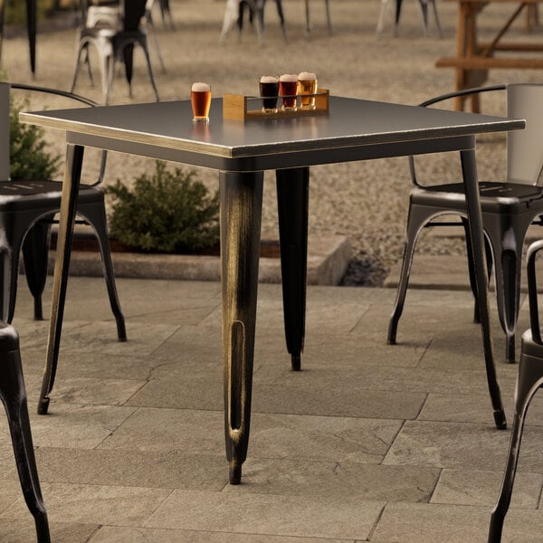 A Lancaster Table & Seating distressed gold outdoor table with glasses of beer on it.