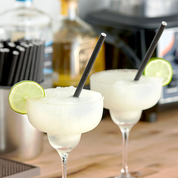 Two glasses with a black Aardvark Giant paper straw in a drink on a table with a lime wedge