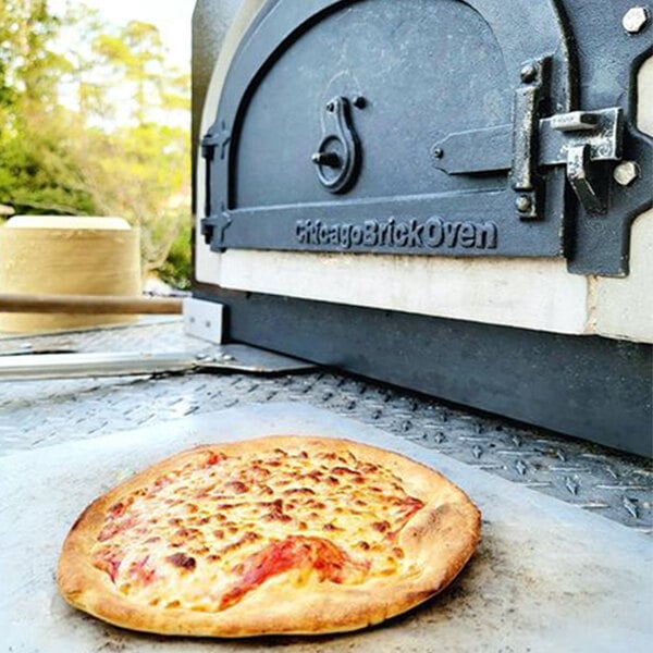A cheese pizza on a pan being cooked in a Chicago Brick Oven Tailgater Pizza Oven.