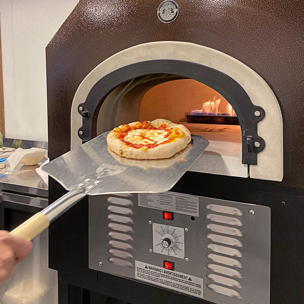 A hand uses a metal spatula to remove a pizza from a Chicago Brick Oven.