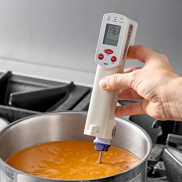 A hand using a Cooper-Atkins digital infrared thermometer to check the temperature of soup.