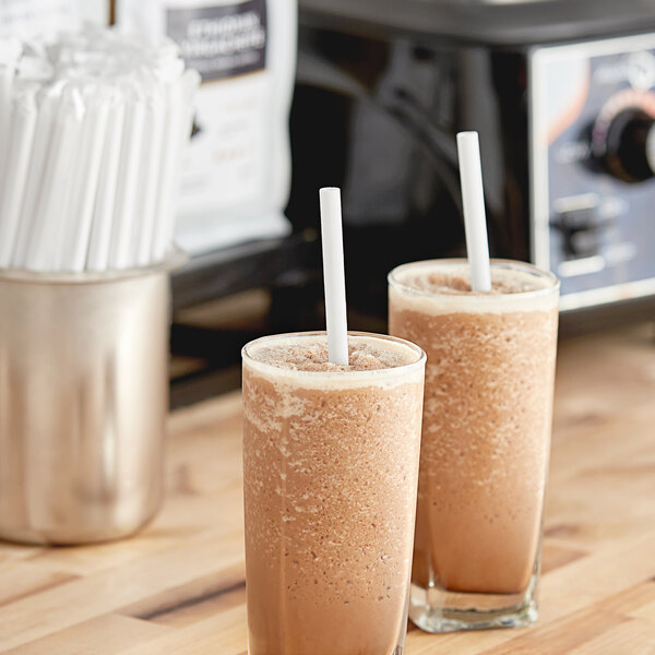 Two glasses of brown liquid with Aardvark white paper straws on a table.