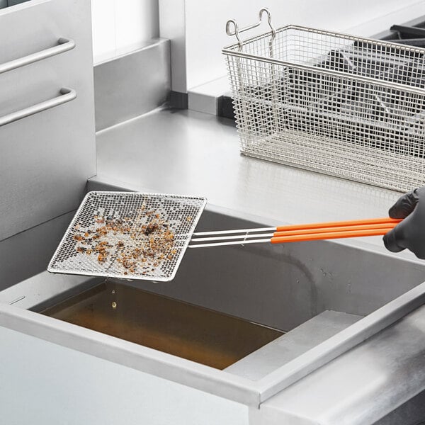 A person in black gloves using a Fryclone mesh skimmer to remove food from a fryer.