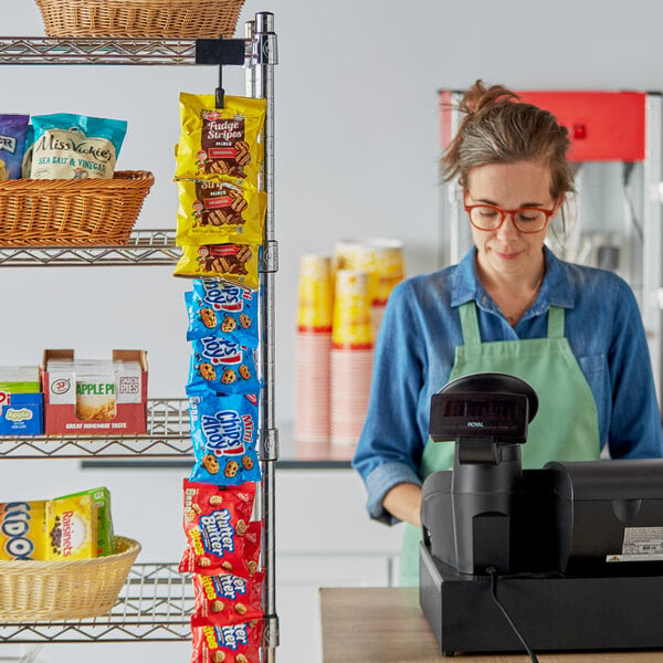 A woman wearing an apron using a Choice hanging chip rack behind a convenience store counter.