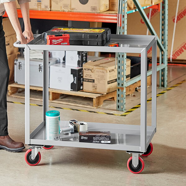 A man standing next to a Lavex steel utility cart with two trays.