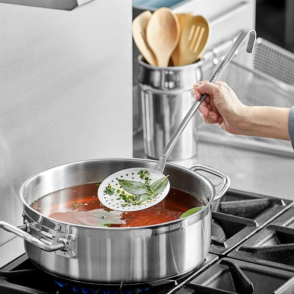 A hand using a Vollrath round skimmer to stir soup in a pot.