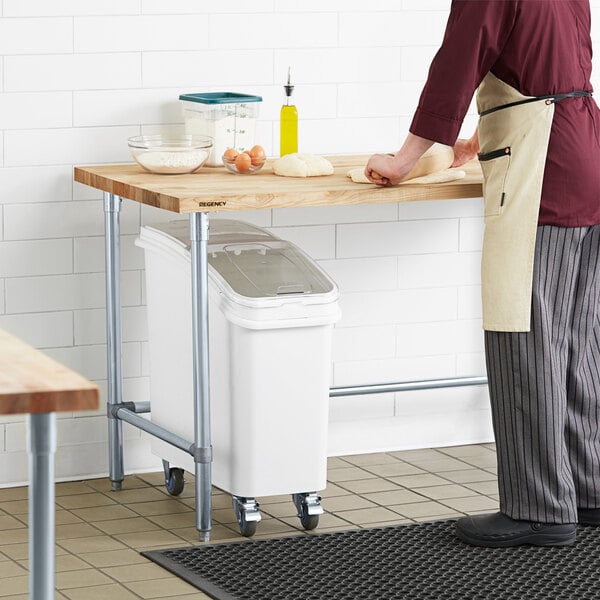 A man in a chef's outfit rolling dough on a Regency wood top work table.