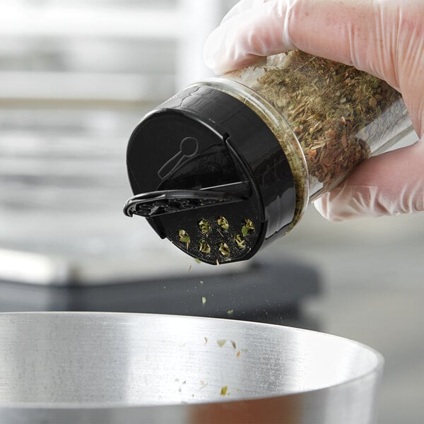 A hand using a black dual flapper spice lid to sprinkle herbs on a salad.