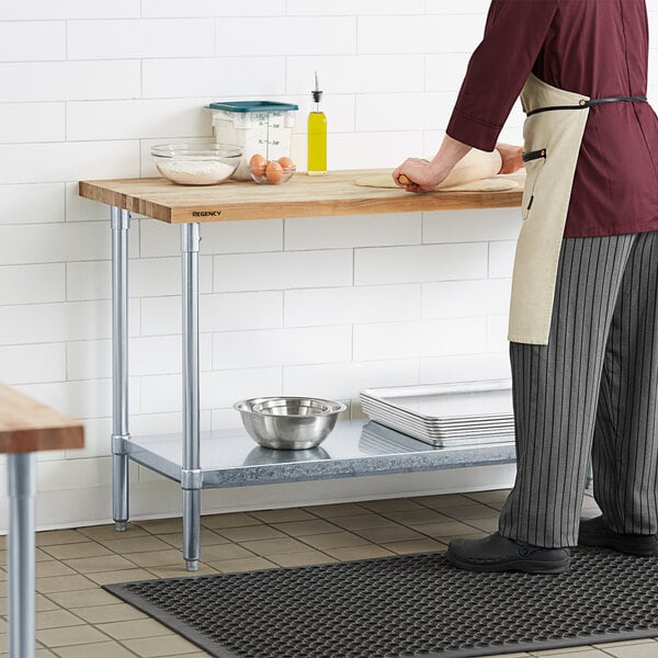 A person in a chef's uniform using a Regency wood top work table in a professional kitchen.