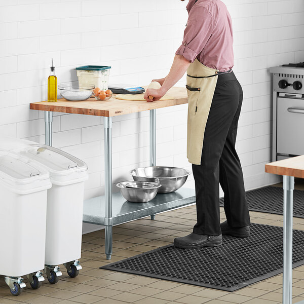 A man standing at a Regency wood top work table in a professional kitchen.