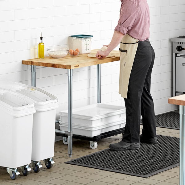 A man in an apron using a Regency wood top work table in a professional kitchen.