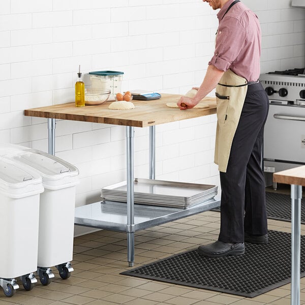 A man in an apron rolling out dough on a Regency wood top work table in a kitchen.