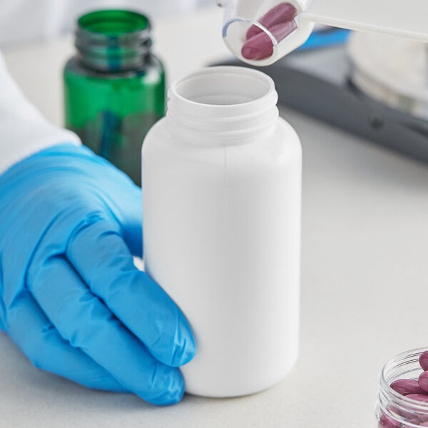 A gloved hand pouring a pink pill into a white 300cc HDPE packer bottle.