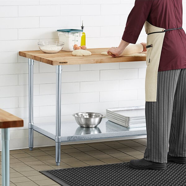 A person in a chef's uniform rolling dough on a Regency wood top work table with a galvanized base.