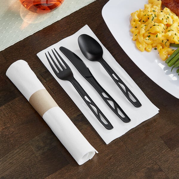 A table with a FashnPoint white napkin and 3-piece black plastic cutlery pre-roll.