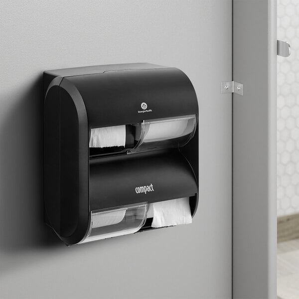 A black and white Compact by GP Pro Quad Coreless Roll high capacity toilet paper dispenser on a wall.