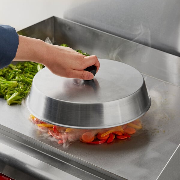A person holding a Choice aluminum basting cover over a pan of vegetables.