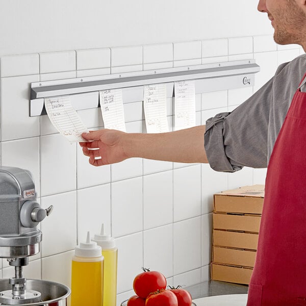 A man in a red apron using a Choice Stainless Steel Wall Mounted Ticket Holder to hold a paper.