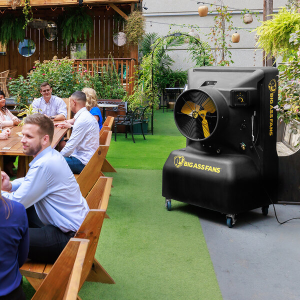 A group of people sitting at a table in a garden with a Big Ass Fans Cool-Space 350 industrial cooler.