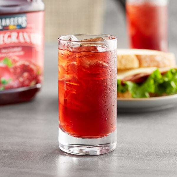 A glass of Langers Pomegranate Juice with ice and a sandwich on the side.