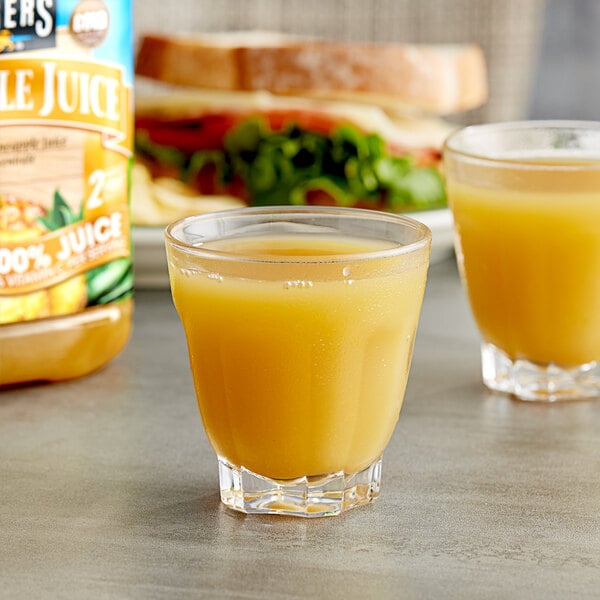 Two glasses of pineapple juice next to a sandwich on a table.