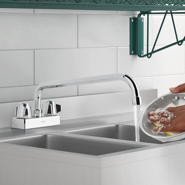 A person using a 1.8 GPM deck-mount faucet with a 12" swing spout to wash dishes in a sink.