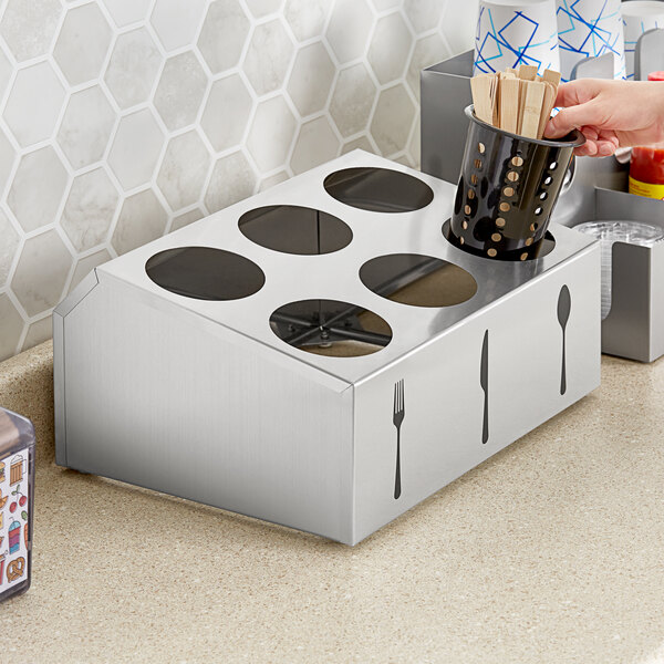 A silver box with six circles and a black container with utensils in it.